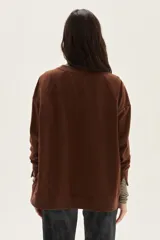 Buzo oversize de felpa color marrón con bordado frontal de una flor estilizada y la palabra "Muse" escrita en cursiva en color celeste.