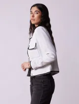 Chaqueta de tweed negra marca Nanette, con escote a la base, abertura central con botones, bolsillos delanteros, aplique de botones perlados en los puños, ribete en contraste blanco y forro interno.