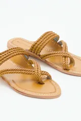Sandalia plana de cuero color tostado, con diseño de tiras trenzadas que se cruzan sobre el empeine y sujetan el dedo. Presenta costuras decorativas en el contorno de la plantilla.