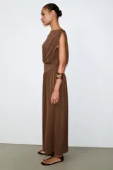 Vestido largo sin mangas de cuello redondo, confeccionado en tejido drapeado con detalle de cintura tipo fajín en el mismo material.