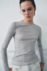 Top de punto fino y semitransparente color gris claro, con cuello redondo y manga larga.