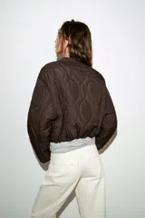 Cazadora corta acolchada de color negro, con cuello redondo, manga larga y cierre frontal con botones. Presenta un diseño de costuras geométricas y bolsillos laterales de vivo.