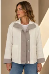 Campera marrón de lino con diseño bicolor, con una franja central gris claro que incluye botones de nácar. Cuenta con cuello alto, mangas largas con puños grises, bolsillos frontales aplicados y silueta amplia.