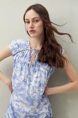 Vestido largo con estampado geométrico en tonos azul, marrón y beige. Tiene escote en V con lazos ajustables, mangas cortas y corte holgado.