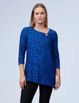 Blusa azul con estampado de círculos negros, de tejido texturado con escote en V descentrado y aplique de aro metálico.