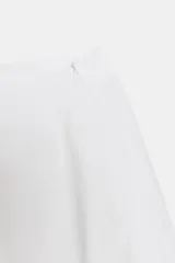 Falda midi blanca de tiro medio con bolsillos delanteros y bajo asimétrico. Cierre lateral con cremallera oculta.