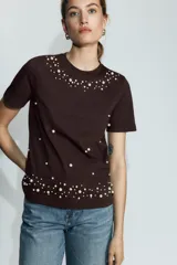 Camiseta de cuello redondo y manga corta en color marrón oscuro, con detalle de aplicaciones de perlas distribuidas en el cuello y en el ruedo.