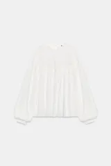 Camisa blanca de manga larga con cuello redondo y diseño abullonado, con detalle de bordados y encaje en la parte frontal y cierre de botón en la espalda.