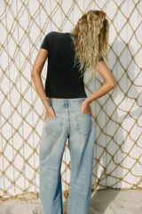 Jeans de tiro bajo y corte wide leg, confeccionados en denim de color celeste claro con lavado desgastado. Presentan detalles de roturas y aplicación de tachas metálicas en los laterales y bolsillos delanteros. Cierre frontal con cremallera y botón.