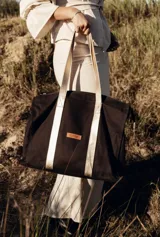 Bolso tipo tote bag negro con detalles dorados en las asas y en el logo.