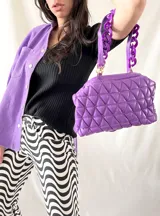 Cartera morada acolchada con diseño de rombos y asa de cadena gruesa.