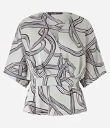Blusa de tela satinada color gris con estampado abstracto en negro y blanco, escote en V cruzado, mangas cortas y cintura elastizada.