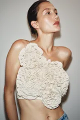 Top crop color blanco hueso con escote recto y hombros descubiertos. Presenta una aplicación de flores tridimensionales en relieve cubriendo toda la parte delantera.