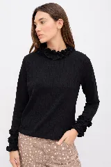 Polera negra de manga larga con volados decorativos en el cuello y en los puños. Presenta un diseño de calce relajado y tejido suave con textura acanalada.