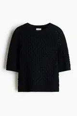 Remera de punto pointelle suave de color negro, con cuello redondo ribeteado acanalado y mangas raglán al codo. Presenta remate acanalado en mangas y bajo.