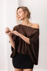 Blusa fluida de color marrón, con diseño holgado, escote bote que deja un hombro al descubierto y mangas anchas y cortas.