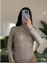 Body de manga larga y cuello alto, color tostado, con diseño de espalda descubierta y tejido texturado con patrón geométrico tridimensional.