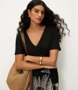 Vestido corto negro de viscosa y lino, con escote en V, mangas cortas y estampa gráfica de follaje blanco en la parte inferior, complementada con franjas horizontales en el ruedo.