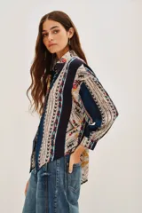 Camisa de manga larga con estampado étnico multicolor, cuello clásico y cierre frontal con botones. Presenta un diseño de rayas verticales con patrones geométricos y detalles en tonos azules, rojos, amarillos y beige.
