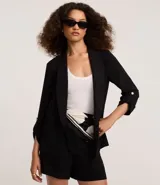 Blazer negro confeccionado en tejido airflow, con solapa en el cuello y abertura total. La prenda tiene martingalas en los puños, que son tiras con botones.