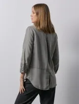 Camisa gris de tencel con cuello con solapa, escote en V y abertura central con botones. Largo de manga regulable con presilla y botón. Ruedo en espalda con tajo.