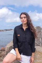 Camisa de lino color negro, de corte holgado, con cuello clásico, cierre frontal de botones y dos bolsillos delanteros con parche de cuero con logo.