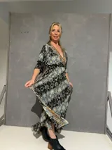 Vestido largo cruzado al frente de seda estampado en tonos azules, negros y dorados, con escote en V ribeteado, mangas 3/4 fluidas y elástico en la parte trasera de la cintura.