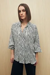Camisa de calce relajado con estampado lineal irregular en blanco y negro. Presenta cuello clásico, abotonadura frontal, mangas largas con puños camiseros y detalles de recortes verticales en el frente.