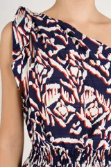 Vestido largo de diseño asimétrico con un solo hombro y detalle de lazo en el tirante. Presenta cintura elastizada fruncida y una falda fluida con estampado geométrico en tonos azul marino, blanco y rojo.