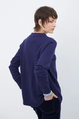 Cardigan de punto color beige, con cuello camisero, cierre frontal de botones y bolsillo aplicado en el pecho. Presenta mangas largas con puños acanalados y un corte recto y holgado.