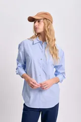 Camisa celeste con rayas verticales blancas, de corte clásico, con cuello camisero, manga larga y bolsillo en el pecho.