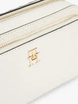 Cartera tipo cámara Tommy Hilfiger color beige, con acabado texturizado, monograma TH en bajo relieve y herrajes dorados. Cuenta con correa cruzada ajustable y extraíble, cierre de cremallera y un bolsillo exterior.