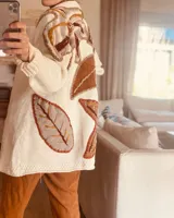 Cárdigan de lana color crudo con apliques de hojas bordadas en tonos marrones, naranjas y amarillos. Corte holgado y largo a la cadera.