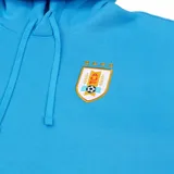 Hoodie Nike celeste con capucha y bolsillo canguro frontal. Presenta el logo de Nike en blanco en el pecho izquierdo y el escudo de la Asociación Uruguaya de Fútbol (AUF) en el lado derecho.