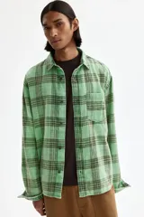 Camisa H&M de sarga de algodón verde con diseño de cuadros oscuros, cuello inglés, un bolsillo en el pecho y cierre frontal de botones.