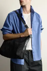 Bolso de hombro tipo shopper en color negro, con diseño liso y cierre magnético. Cuenta con un bolsillo interior con cremallera y asa ajustable.