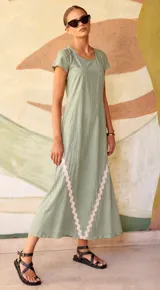 Vestido largo color verde con cuello redondo y mangas cortas. Presenta un diseño de corte recto con detalles de ondas en color rosado claro en la parte inferior delantera.