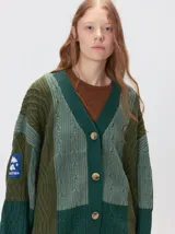 Cardigan oversize de tejido de punto grueso con diseño de bloques de color en tonos beige y marrón. Presenta cuello en V, cierre frontal con botones, mangas largas abullonadas y parches decorativos en el pecho y el hombro.