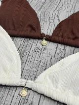 Corpiño de bikini tipo triángulo, con textura acanalada y tirantes regulables. Presenta un pequeño dije metálico en el centro.
