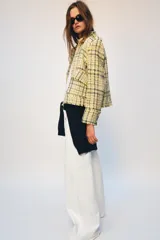 Chaqueta de corte recto confeccionada en tejido con textura de cuadros en tonos amarillos, blancos y negros. Presenta cuello solapa, cierre frontal con botones ocultos, bolsillos de plastrón con solapa en el delantero y mangas largas con puños abotonados.