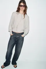 Chaqueta de punto color beige claro, de cuello redondo y manga larga abullonada con puño ajustado. Cierre frontal cruzado con botones plateados.