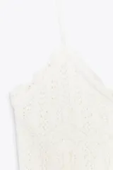 Top corto blanco con tirantes finos y escote en pico. Tejido con diseño calado de patrón geométrico y bordes festoneados.