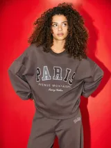 Buzo color chocolate brown con estampado frontal que dice "PARIS AVENUE MONTAIGNE Luxury Fashion". Tiene puños y ruedo acanalados.