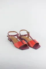 Sandalias de cuero con diseño bicolor en tonos bordó y rojo, con taco cuadrado bajo de 2 cm, punta cuadrada, tira frontal en T y tira ajustable al tobillo con hebilla metálica.