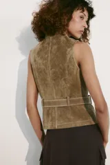 Chaleco de gamuza color marrón, con cuello alto, cierre frontal de cremallera y trabillas con hebilla a los lados de la cintura.