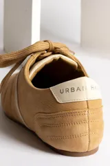 Zapatillas bajas color crema con cordones y suela marrón.