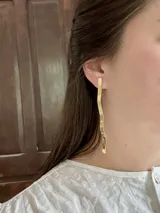 Set de accesorios compuesto por un brazalete rígido abierto, un collar con dije de sol radiante, un par de caravanas onduladas y un par de caravanas tipo fleco, presentados en un sobre de cuero con costuras artesanales.