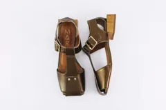 Sandalias de cuero color bronce, con diseño de punta cuadrada, taco cuadrado símil madera y tira ajustable con hebilla en el tobillo.