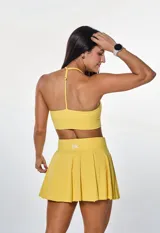 Conjunto deportivo compuesto por un top con cuello halter y una pollera short con diseño plisado, ambos en color amarillo.