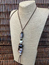 Colgante largo con cordón de cuero marrón y cuentas de piedra natural en tonos marrones, blancos y grisáceos, intercaladas con pequeñas esferas metálicas.